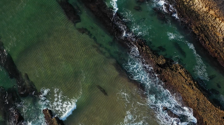 Aerial view of a rocky coastline with turquoise water, gentle waves, and patterned sand formations. The natural shoreline landscape introduces Perl Haven’s 2025 Responsible & Sustainable Portfolio Supplement and its sustainability reporting highlights.